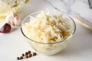 Glass bowl with tasty sauerkraut, garlic and peppercorns on white background, closeup