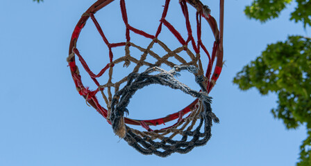 Old basketball hoop with worn net against blue sky