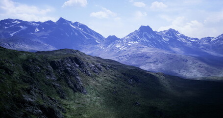 Vast mountains rise majestically against a bright blue sky, showcasing rugged peaks and lush green valleys. Soft sunlight highlights the stunning terrain, inviting adventure and exploration.