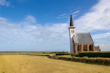 Typical landscape of Texel island with small village and picturesque church (Hervormde kerk) under blue sky and white clouds, A little town on the wadden islands, Den Hoorn, Noord Holland, Netherlands