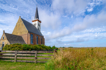 Typical landscape of Texel island with small village and picturesque church (Hervormde kerk) under blue sky and white clouds, A little town on the wadden islands, Den Hoorn, Noord Holland, Netherlands