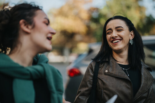 Two happy women enjoy a lively conversation and share laughter outside on a sunny day, showcasing friendship and connection.