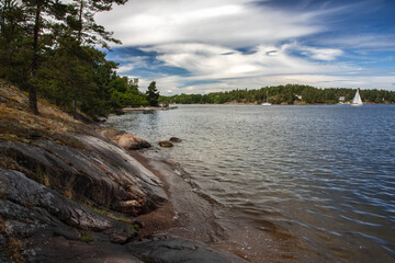 Rocky shore in a sea bay under a synth cloudy sky on a summer day