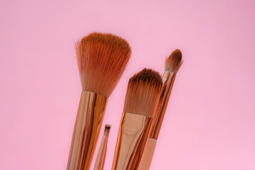 Set of makeup brushes with rose gold handles against a soft pink background. The fluffy bristles...