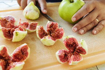 Close-up shot of peeled figs cut up into quarters, showing the red seeds inside, a person's hand on...