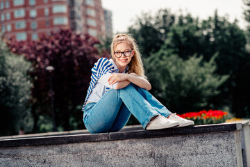Beautiful girl enjoying a sunny day outdoors, sitting casually in trendy casual attire in a vibrant urban park setting