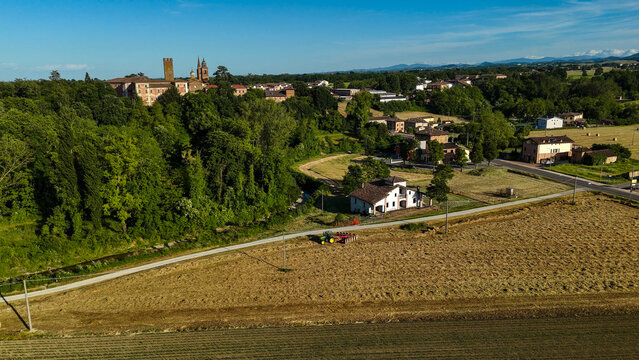 Aerial panorama overlooking Govone village in Piedmont, revealing verdant agricultural landscape, residential zones, and distant Alpine mountain range