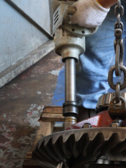 A mechanic uses an air impact wrench to work on crown gear differential assembly. This image...