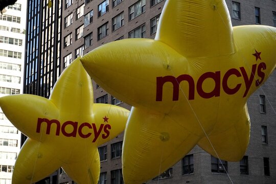 Two yellow balloons shaped as stars with the logo of Macy's department store flying on a wagon in the famous annual Thanksgiving Day parade through the streets of Manhattan, New York.