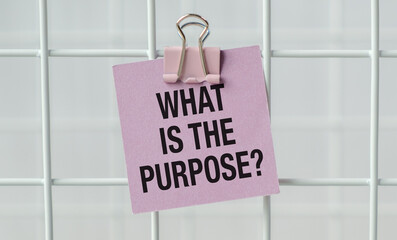 A pink piece of paper with a clip holding it to a white metal surface. The paper says What is the...