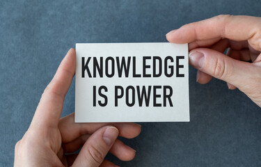 Knowledge is Power close up of a phrase being typed and centered on paper card in hand on gray background