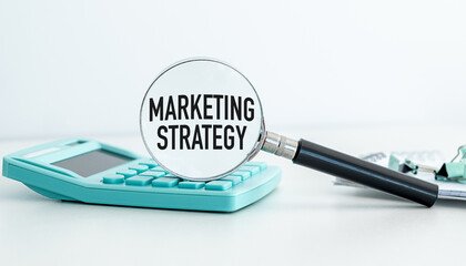 Marketing Strategy text on magnifying glass on calculator on white background