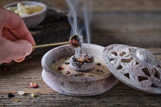 Woman&rsquo;s hand placing incense on burning charcoal in a ceremonial incense bowl