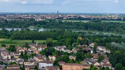 Fototapeta premium Aerial panorama revealing Castelvetro Piacentino, Cremona's Torrazzo tower rising above Po river valley under cloudy skies