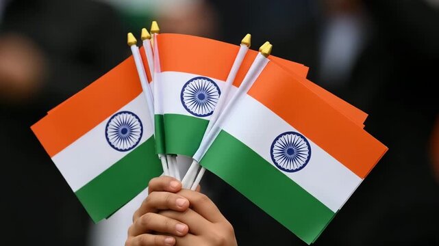 Hands display mini Tiranga flags symbolizing patriotism during a cultural event attended by diverse individuals in a vibrant setting