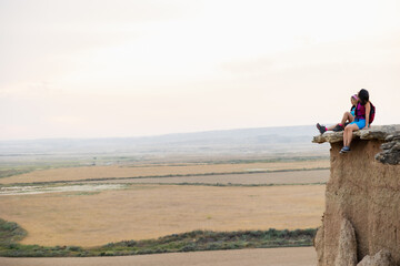 Female hikers sitting on cliff edge overlooking vast rural valley. Lifestyle. Hiking. Bardenas.