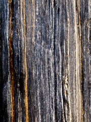 Close-up of a rock surface with vertical striations in shades of black, gray, and gold.
