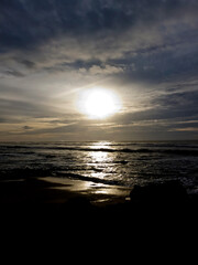 A bright sun shining over the ocean with dark clouds in the sky.