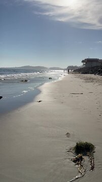 Vertical video of California beach in Santa Barbra showing ocean waves sandy coast sunlight reflections and people walking along the shoreline in summer.