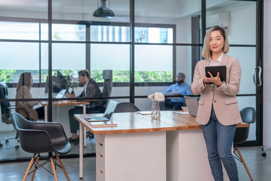 portrait asian female company employee using tablet computer working at table in workplace,business employees on office work - Powered by Adobe