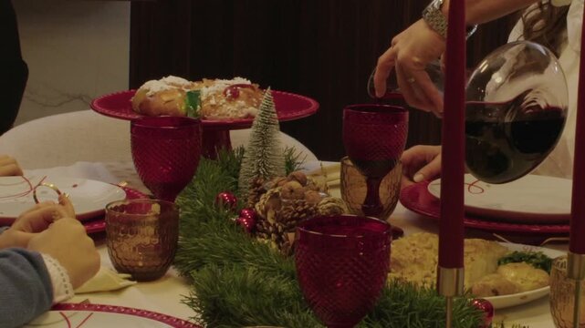 Christmas dinner table with red glasses, bolo rei cake, and wine being poured
