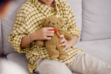 Close-up of Asian boy’s hands gently holding teddy bear with red ribbon during therapy session,...