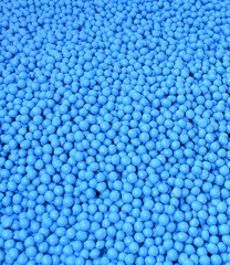 A fragment of a multitude of small, bright blue balls tightly packed together. Processed sugar beet seeds before sowing. Has a smooth, shiny surface and a textured background