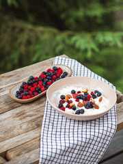 Bowl with cottage cheese and berries served outdoors on a wooden table with napkin in the forest.