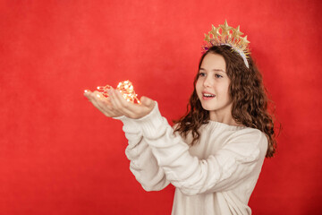 Charming girl in a festive outfit on a red background holding a bright garland in her hands, New...