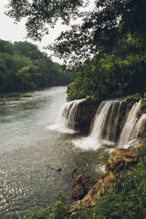 Fototapeta premium Scenic view of waterfalls cascading into river flowing through lush green forest, creating a tranquil and picturesque landscape