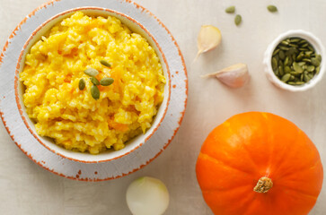 Pumpkin risotto in a white and orange bowl with ingredients on a gray table. Italian dish concept. Autumn food. Selective focus. Horizontal orientation. Top view.