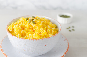 Pumpkin risotto in a white and orange bowl with seeds on a gray table. Italian dish concept. Autumn food. Selective focus. Horizontal orientation. Copy space