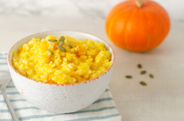 Pumpkin risotto in a white and orange bowl on a striped napkin on a gray table. Italian dish concept. Autumn food. Selective focus. Horizontal orientation. Copy space