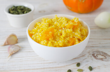 Pumpkin risotto in a white bowl with ingredients on a wooden table. Italian dish concept. Autumn food. Selective focus. Horizontal orientation.