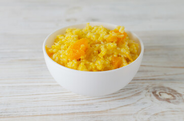 Pumpkin risotto in a white bowl on a wooden table. Italian dish concept. Autumn food. Selective focus. Horizontal orientation.