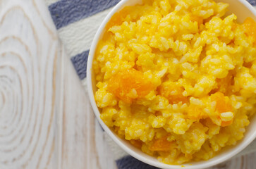 Pumpkin risotto in a white bowl on a striped napkin on a wooden table. Italian dish concept. Autumn food. Selective focus. Horizontal orientation. Copy space. Top view
