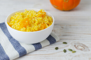 Pumpkin risotto in a white bowl on a striped napkin on a wooden table. Italian dish concept. Autumn food. Selective focus. Horizontal orientation. Copy space