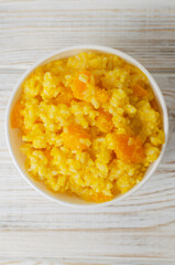 Pumpkin risotto in a white bowl on a wooden table. Italian dish concept. Autumn food. Selective focus. Vertical orientation. Top view