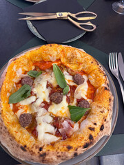 Traditional Neapolitan pizza with tomato, mozzarella, basil and eggplant, served with Italian polpette meatballs on a table, scissors for cutting, top view..