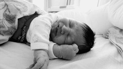 Newborn baby sleeping peacefully with a slight grimace, showing gentle hand movements in a...