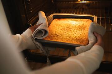 Culinary and people. Homemade lemon cake in a baking pan in the domestic oven with warm light. Process of making and baking citrus pie at the modern kitchen. Homemade food cooking. Close up.
