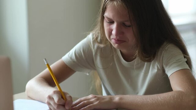 Teen girl student crying while writing and doing homework. Kid tired and unhappy in her studying