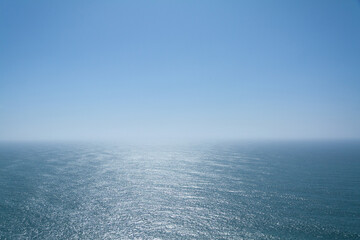 Sunlight reflects and glitters on the vast, calm blue ocean, clear blue sky at the horizon at Cape Roca, Portugal, the westernmost point of continental Europe. Abstraction Wallpaper. Blue background
