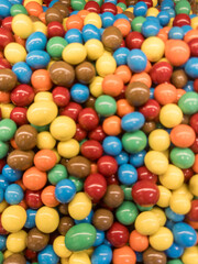 Colorful pile of candy coated chocolate sweets in assorted bright colors. Close-up background texture of multicolored round candies, perfect for food and confectionery themes