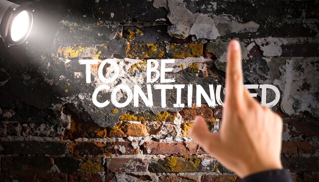 A hand points to the words "To Be Continued" written on a weathered brick wall. A spotlight illuminates the words