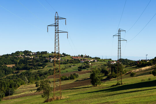 A rural Italian panorama with two large high voltage electrical pylons stretching across a green landscape.