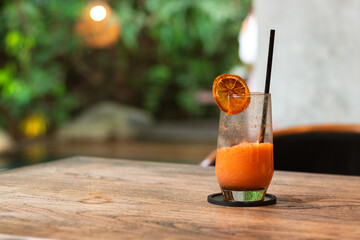 Mixed juice of orange and carrot, on a wooden table with garden background. After edits.