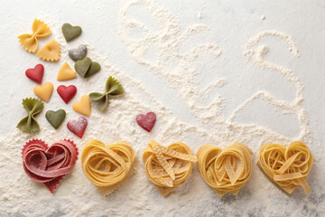 Heart-shaped pasta and noodles in assorted colors arranged neatly on flour-dusted surface