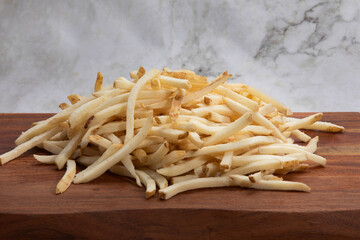 uncooked frozen French fries on wooden board and white marble background