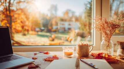 Cozy autumn atmosphere of home office workspace, panoramic view on sunny day, golden park and leaf fall, mug of cocoa, bouquet of red leaves, candle, school laptop and notebooks on the table